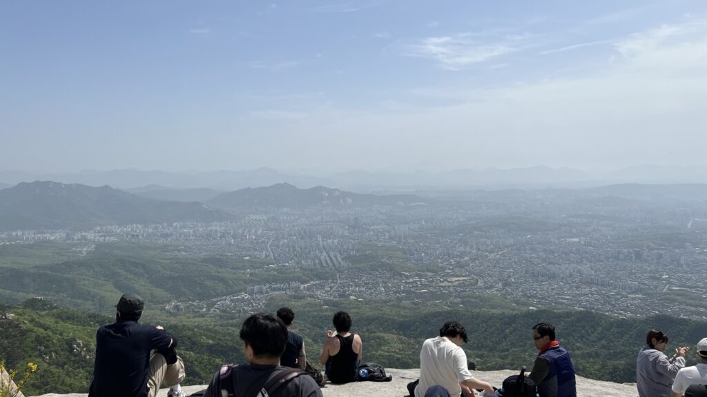 山頂の岩に腰を下ろして眺める。眼下にソウル、奥に山が連なる