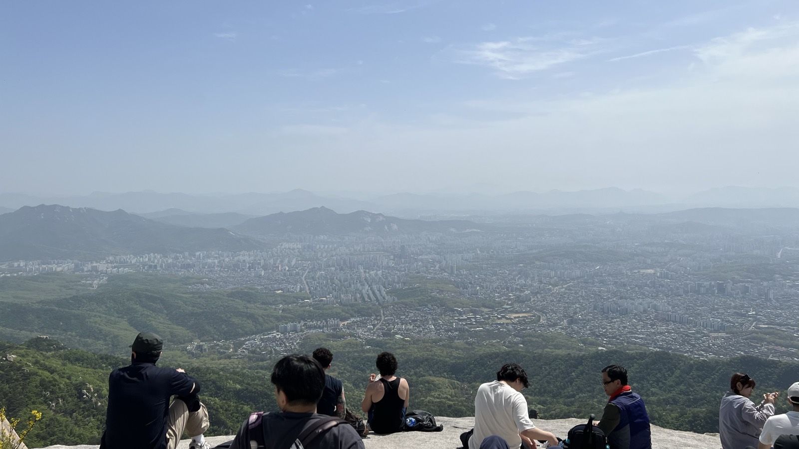 山頂の岩に腰を下ろして眺める。眼下にソウル、奥に山が連なる