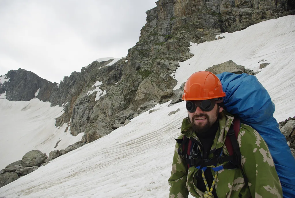 ヘルメットとグレイシャーグラスをかけ、雪の斜面を歩く登山者