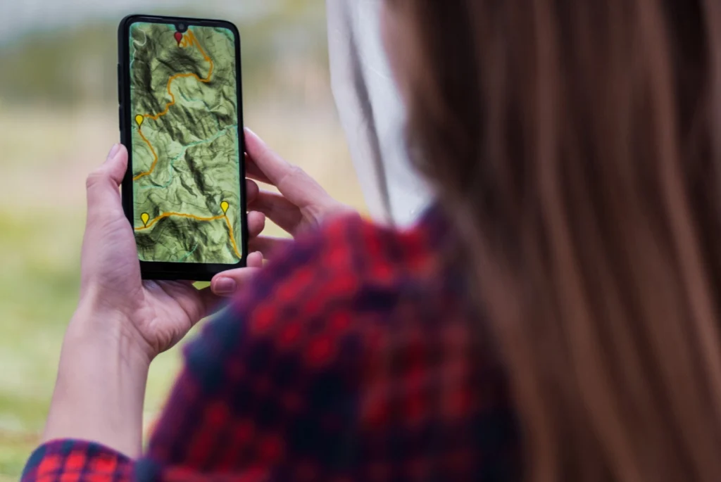 登山道で地形図を表示したスマートフォンを持つ手