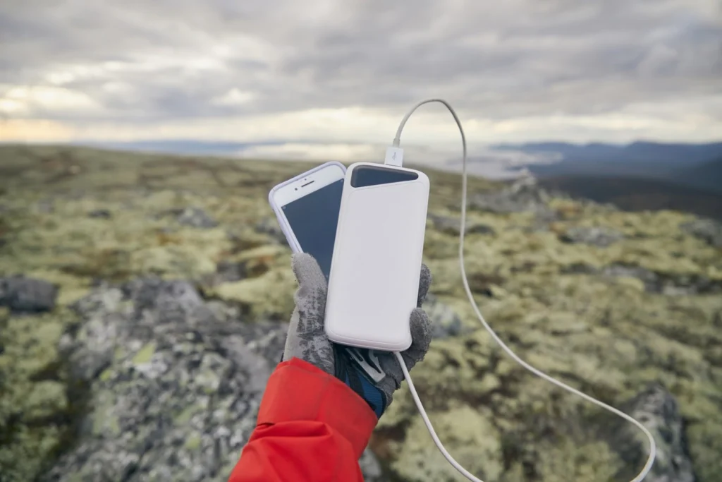 山でモバイルバッテリーとスマートフォンを持つ手
