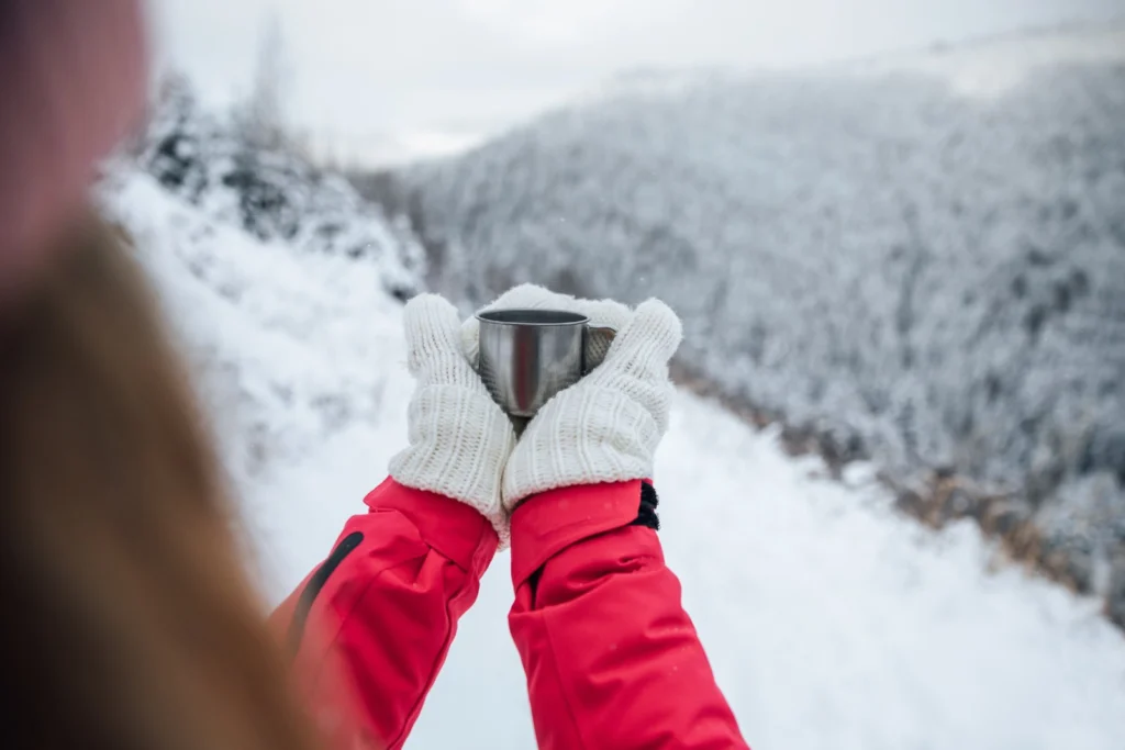 雪の中で手袋をした両手で温かいカップを持つ